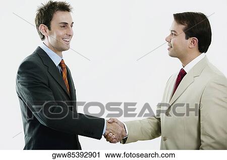 Stock Image - Side profile of two businessmen shaking hands and smiling. Fotosearch