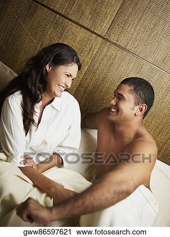 Stock Image - Young couple smiling on the bed and looking at each other. Fotosearch