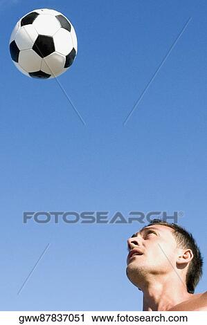 Stock Image - Young man playing with a football on the beach. Fotosearch