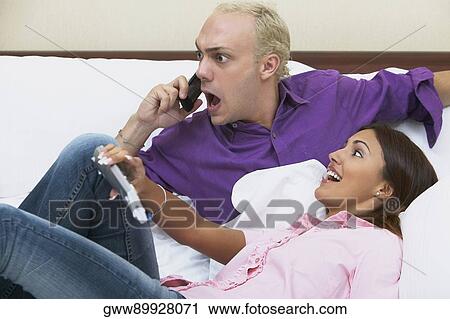Young man using a mobile phone on the bed with a young woman leaning on him View Large Photo Image Stock Image - Young man using a mobile phone on the bed with a young woman leaning on him. Fotosearch