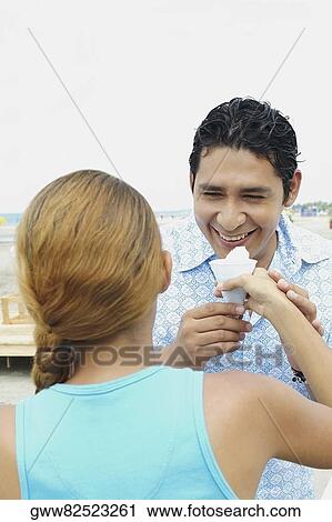 Young woman holding an ice-cream in front of a mid adult man's mouth View Large Photo Image Stock Image - Young woman holding an ice-cream in front of a mid adult man's mouth. Fotosearch