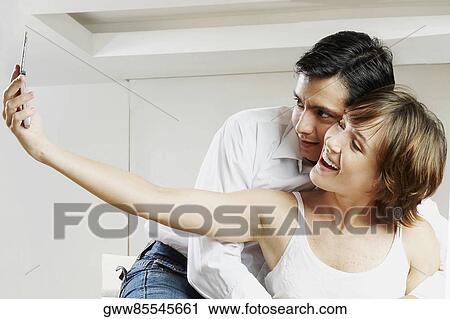 Young woman taking a picture with a mid adult man embracing her from behind View Large Photo Image Stock Image - Young woman taking a picture with a mid adult man embracing her from behind. Fotosearch