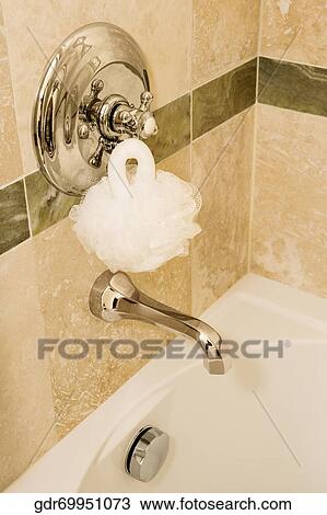 Stock Image - Bath sponge on a faucet over a bathtub. Fotosearch