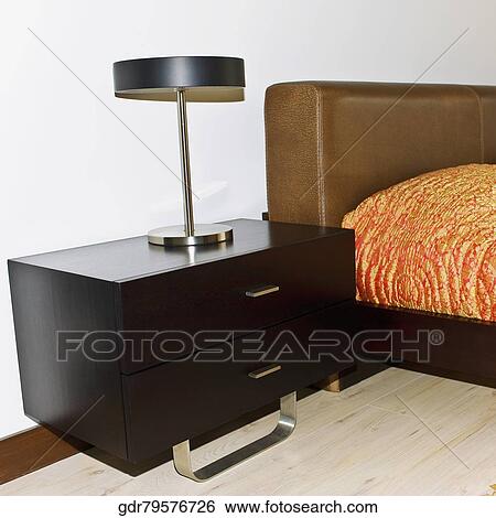 Lamp on a night table beside a bed View Large Photo Image Stock Photograph - Lamp on a night table beside a bed. Fotosearch