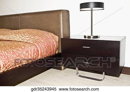 Lamp on a night table beside a bed View Large Photo Image Stock Photography - Lamp on a night table beside a bed. Fotosearch
