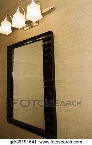 Stock Image - Lamps lit up over a bathroom mirror. Fotosearch