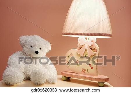 Stock Image - Stuffed toy and a lamp on a night table. Fotosearch