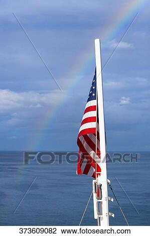 Stock Image - American flag with rainbow in the background. Fotosearch