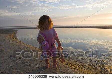 Baby girl carrying dolls on the beach View Large Photo Image Stock Photo - Baby girl carrying dolls on the beach. Fotosearch