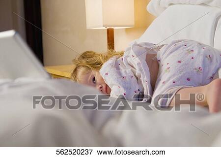 Baby girl lying on the bed and looking at a laptop View Large Photo Image Stock Photo - Baby girl lying on the bed and looking at a laptop. Fotosearch