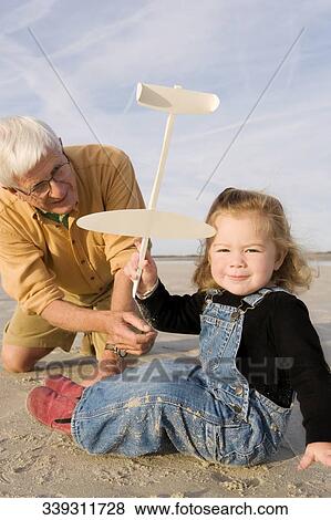 Stock Photo - Baby girl playing with a toy airplane and her grandfather behind her. Fotosearch