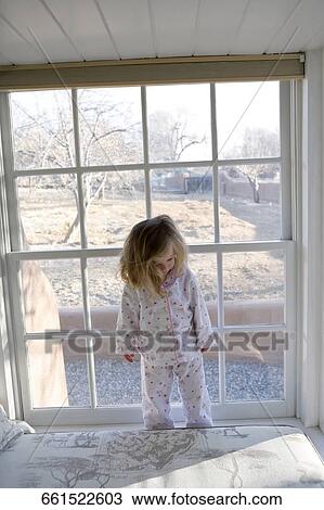 Stock Image - Baby girl standing in front of a window. Fotosearch