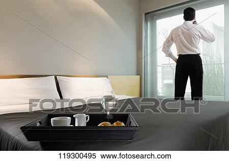 Stock Photography - Breakfast tray on the bed and a businessman looking through the window. Fotosearch
