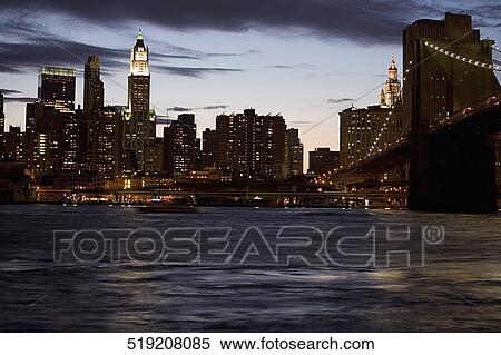 Bridge across a river with buildings lit up in the background at dusk, Brooklyn Bridge, East River, Manhattan, New York City, New York State, USA View Large Photo Image Stock Photography - Bridge across a river with buildings lit up in the background at dusk, Brooklyn Bridge, East River, Manhattan, New York City, New York State, USA. Fotosearch