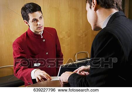 Stock Photograph - Businessman checking a card at hotel reception. Fotosearch