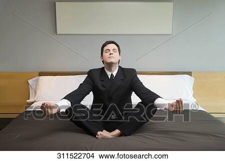 Businessman meditating on the bed in a hotel room View Large Photo Image Picture - Businessman meditating on the bed in a hotel room. Fotosearch