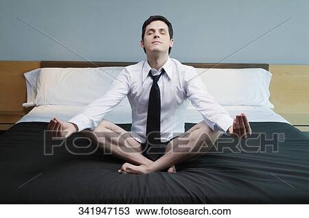 Stock Image - Businessman meditating on the bed in a hotel room. Fotosearch