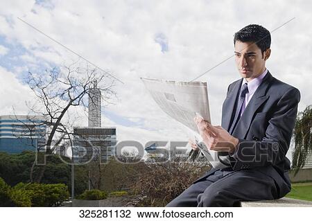 Businessman sitting at the edge of a wall and reading a newspaper View Large Photo Image Stock Image - Businessman sitting at the edge of a wall and reading a newspaper. Fotosearch