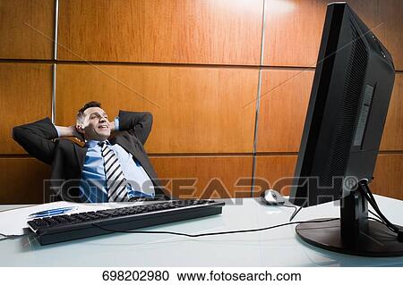 Stock Image - Businessman sitting in an office chair and day dreaming. Fotosearch
