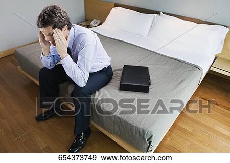 Stock Photo - Businessman sitting on the bed and suffering from a headache. Fotosearch