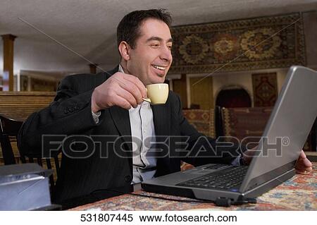 Businessman using a laptop in a restaurant and smiling View Large Photo Image Stock Photography - Businessman using a laptop in a restaurant and smiling. Fotosearch