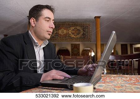 Businessman working on a laptop in a restaurant View Large Photo Image Stock Image - Businessman working on a laptop in a restaurant. Fotosearch