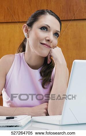 Businesswoman dreaming in front of a laptop with her hand on her chin View Large Photo Image Stock Photography - Businesswoman dreaming in front of a laptop with her hand on her chin. Fotosearch