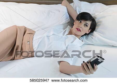 Businesswoman lying on the bed and holding a mobile phone View Large Photo Image Stock Photo - Businesswoman lying on the bed and holding a mobile phone. Fotosearch