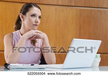 Businesswoman thinking in front of a laptop with her hand on her chin View Large Photo Image Picture - Businesswoman thinking in front of a laptop with her hand on her chin. Fotosearch