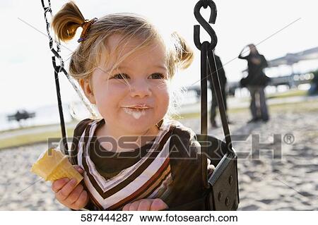 Close-up of a baby girl sitting on a chain swing ride and eating an ice cream View Large Photo Image Stock Photo - Close-up of a baby girl sitting on a chain swing ride and eating an ice cream. Fotosearch