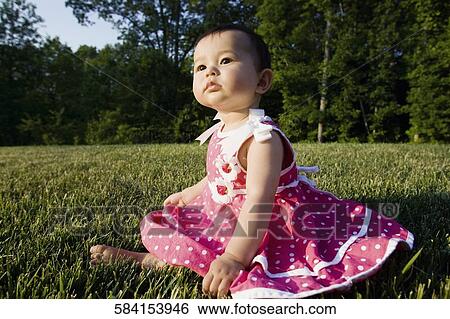 Close-up of a baby girl sitting on grass in a park View Large Photo Image Stock Photograph - Close-up of a baby girl sitting on grass in a park. Fotosearch