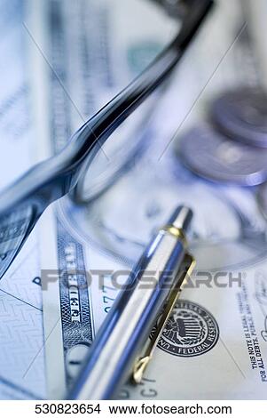 Picture - Close-up of a ballpoint pen with eyeglasses and coins on a paper currency. Fotosearch