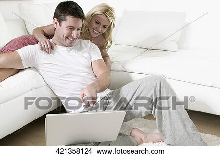 Close-up of a mid adult man smiling with his wife and looking at a laptop View Large Photo Image Picture - Close-up of a mid adult man smiling with his wife and looking at a laptop. Fotosearch