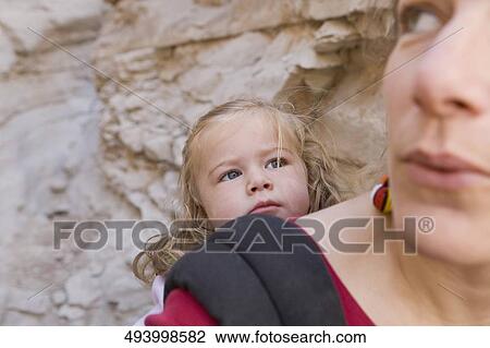 Stock Image - Close-up of a mid adult woman carrying her daughter in a baby carrier. Fotosearch