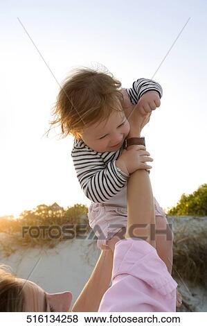 Close-up of a mid adult woman holding her baby girl in air View Large Photo Image Stock Photo - Close-up of a mid adult woman holding her baby girl in air. Fotosearch