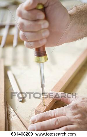 Stock Photo - Close-up of a person's hand tightening a screw with a screwdriver. Fotosearch