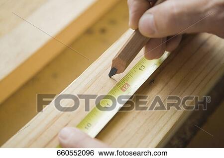 Stock Photograph - Close-up of a person's hands measuring a wooden plank. Fotosearch