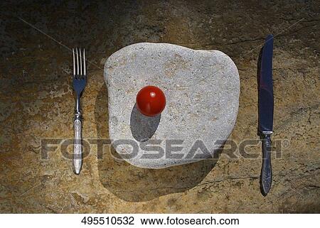 Stock Image - Close-up of a tomato on a stone with a fork and a table knife. Fotosearch