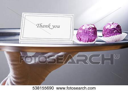 Stock Image - Close-up of a waiter's hand carrying a plate with thank you note and chocolates. Fotosearch