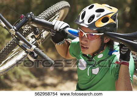 Picture - Close-up of a young man carrying a mountain bike on his shoulders. Fotosearch