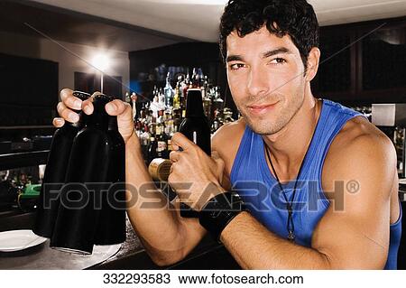 Close-up of a young man sitting at a bar counter and holding beer bottles View Large Photo Image Stock Image - Close-up of a young man sitting at a bar counter and holding beer bottles. Fotosearch