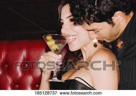Stock Photo - Close-up of a young man sitting on a booth and embracing a mid adult woman. Fotosearch