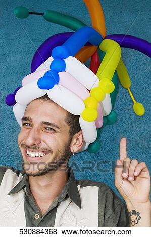 Stock Photo - Close-up of a young man wearing balloons headdress and smiling. Fotosearch