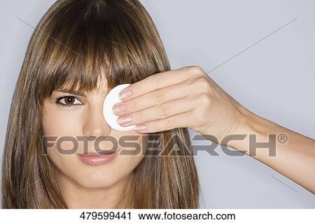 Stock Image - Close-up of a young woman covering her eye with a powder puff. Fotosearch