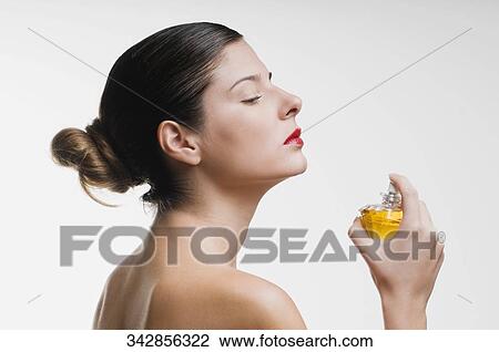 Stock Image - Close-up of a young woman holding a perfume bottle. Fotosearch
