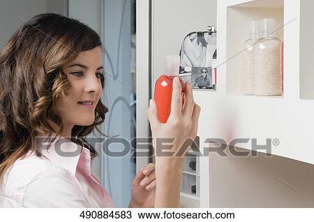 Stock Image - Close-up of a young woman holding a bottle of cosmetics. Fotosearch