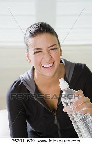 Close-up of a young woman holding a water bottle and smiling View Large Photo Image Stock Photo - Close-up of a young woman holding a water bottle and smiling. Fotosearch