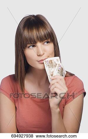 Stock Photo - Close-up of a young woman holding Euro banknotes and thinking. Fotosearch