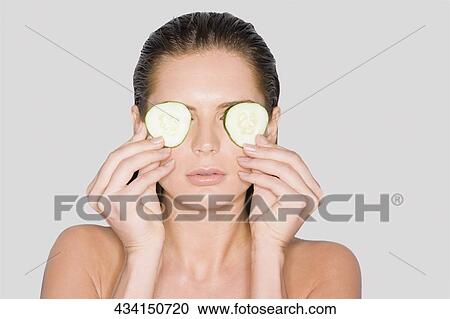Close-up of a young woman holding cucumber slices over her eyes View Large Photo Image Stock Image - Close-up of a young woman holding cucumber slices over her eyes. Fotosearch