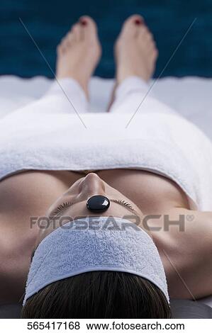 Close-up of a young woman lying on a massage table with a pebble on her forehead View Large Photo Image Stock Photo - Close-up of a young woman lying on a massage table with a pebble on her forehead. Fotosearch